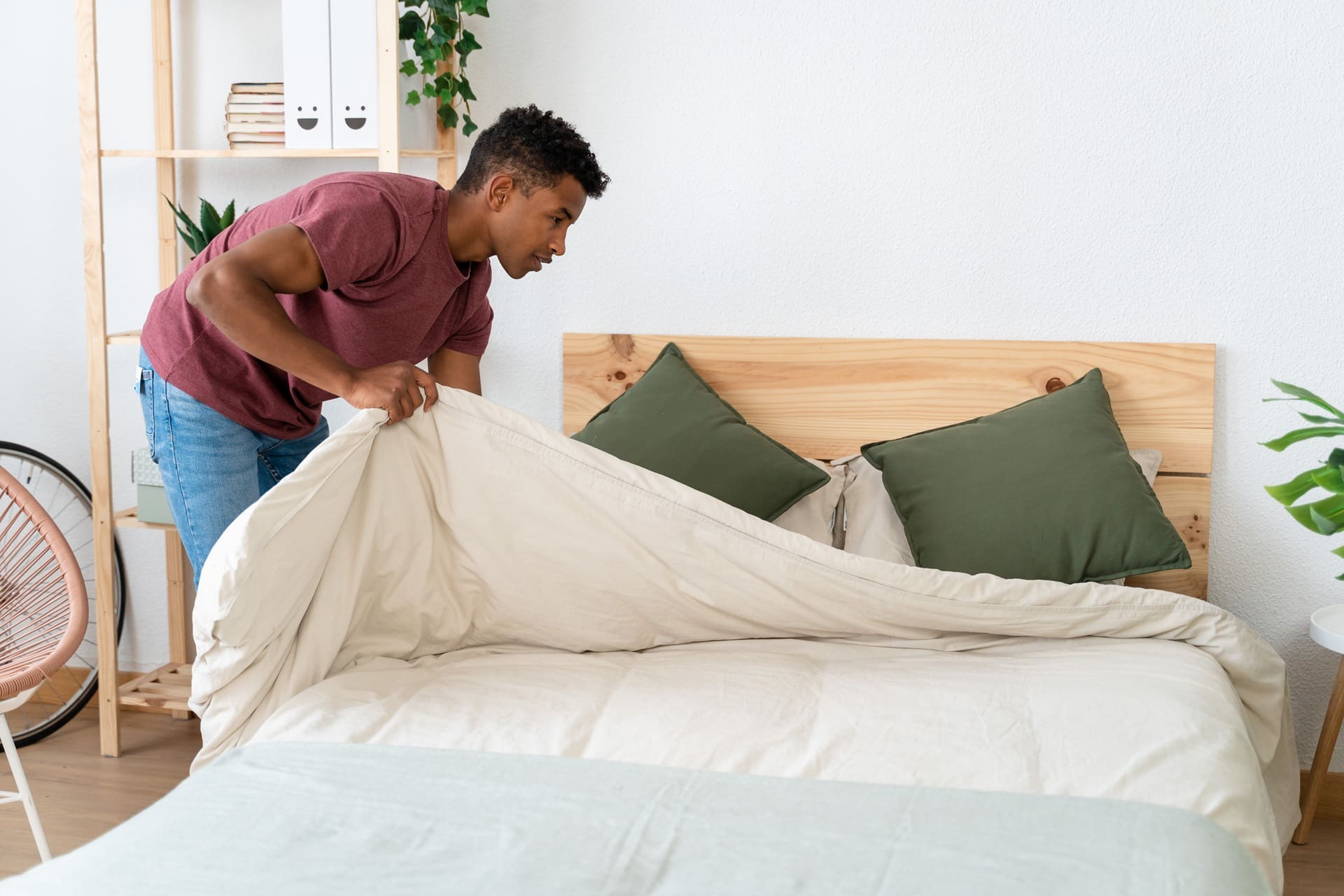 Young man making the bed in his room.